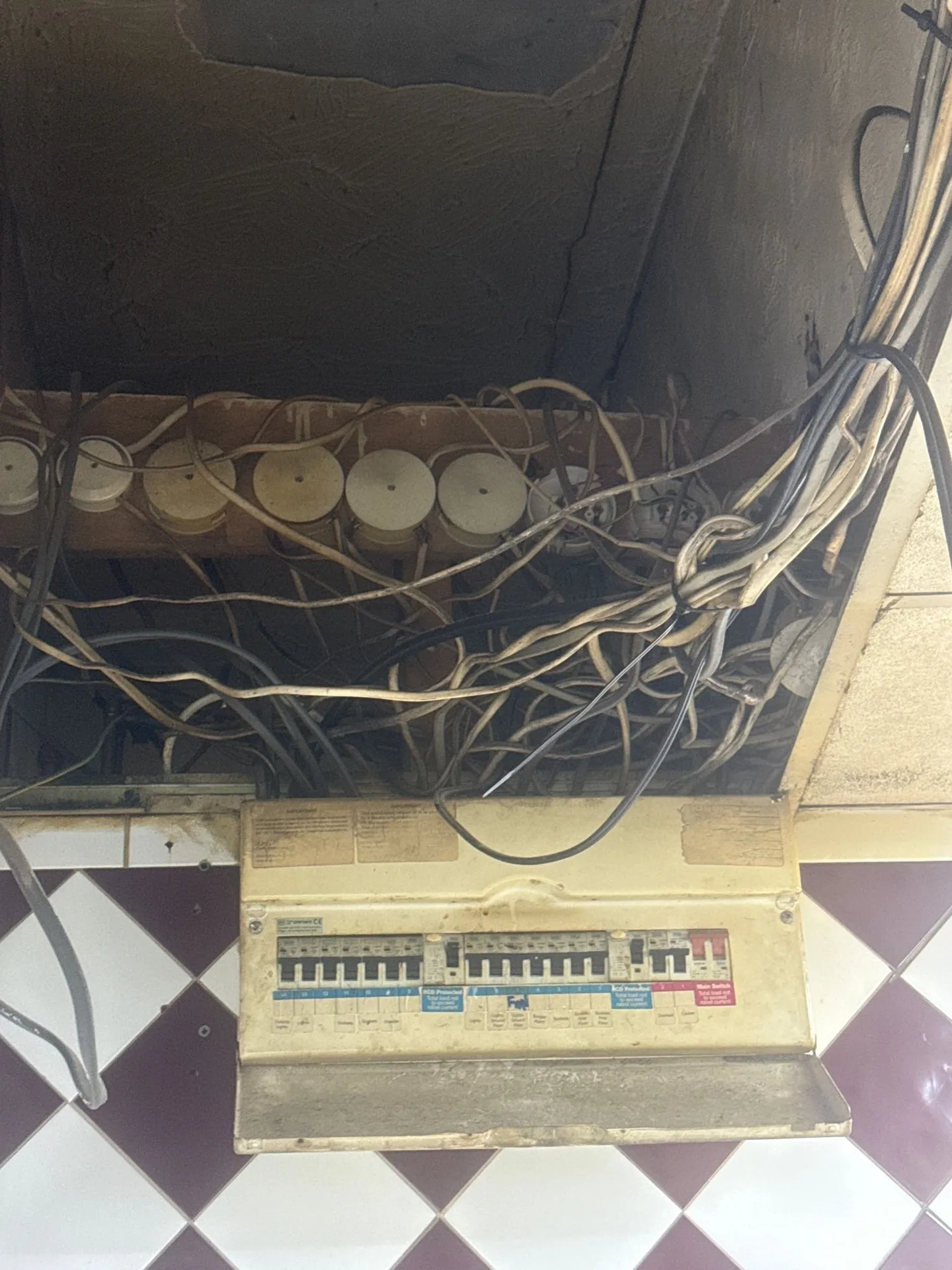 Old split-load consumer unit at the back of a Walthamstow E17 shop with chaotic single-core cabling and exposed copper above