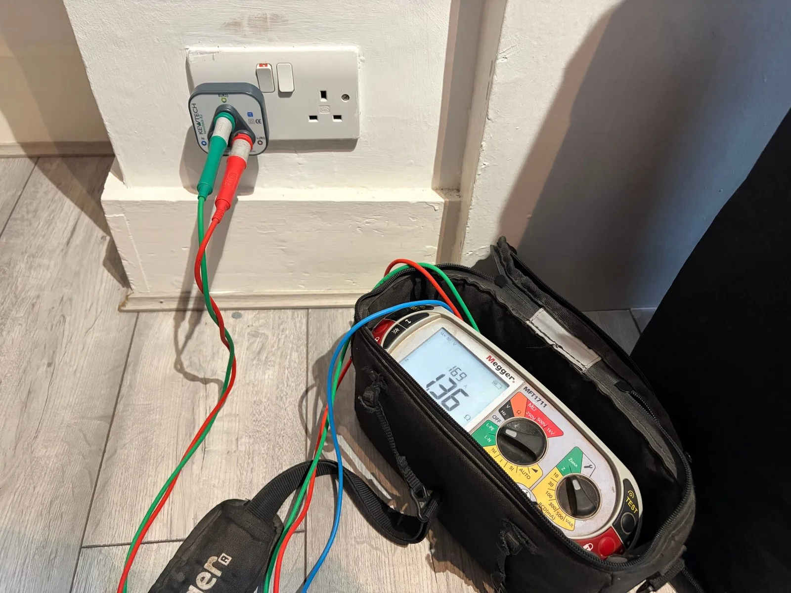Megger MFT1711 multifunction tester showing 1.36 Ω earth-loop impedance reading at a socket via KEWTECH plug-in tester
