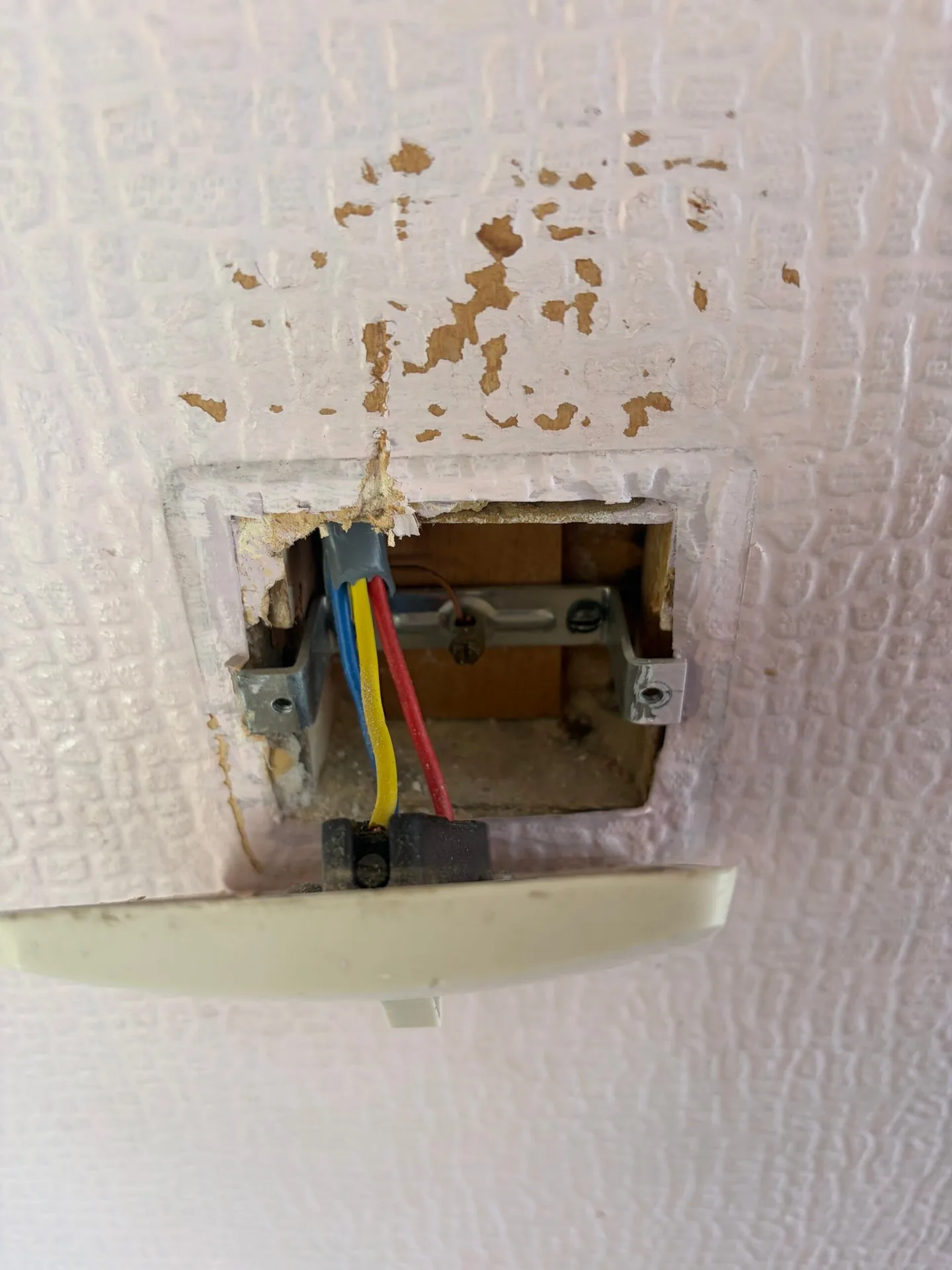 Old single-core insulated cables (red, yellow, blue) inside a damaged wall switch box — no CPC, tinned-copper conductors with degraded insulation